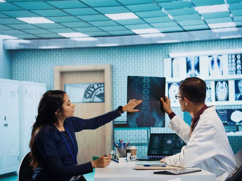Indian general practitioner and nurse examine hospital records and x ray tests, finding diagnosis for a patient. Medical staff reviewing scans and doing healthcare reports with expertise. Camera B.